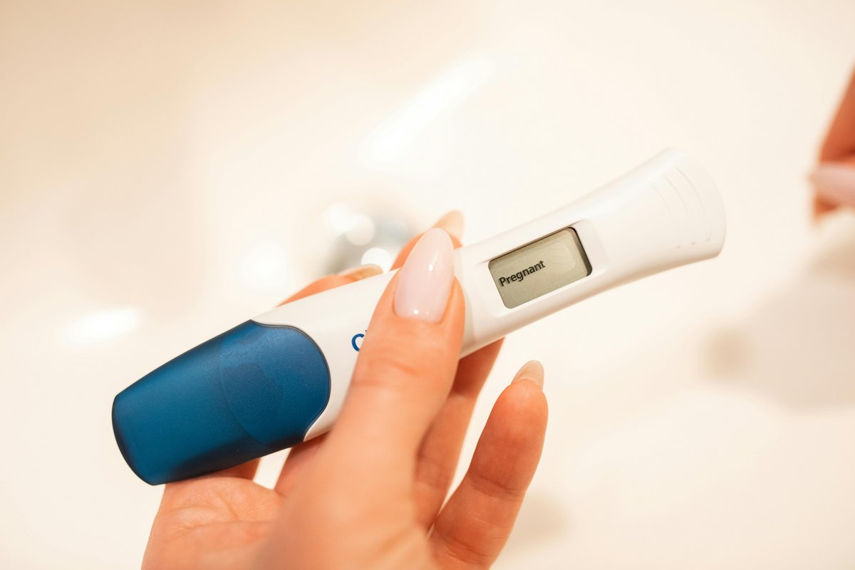 Two hands are holding a positive pregnancy test with the word "pregnant" written on it.