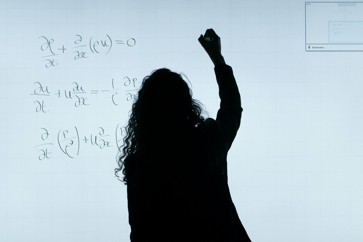 Eine Frau schreibt eine mathematische Gleichung an eine Tafel.