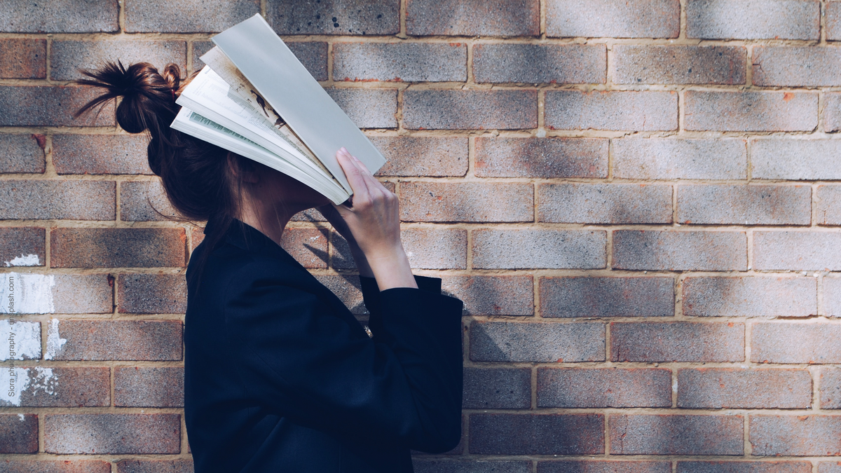 Eine Person hält ein Buch vor ihr Gesicht