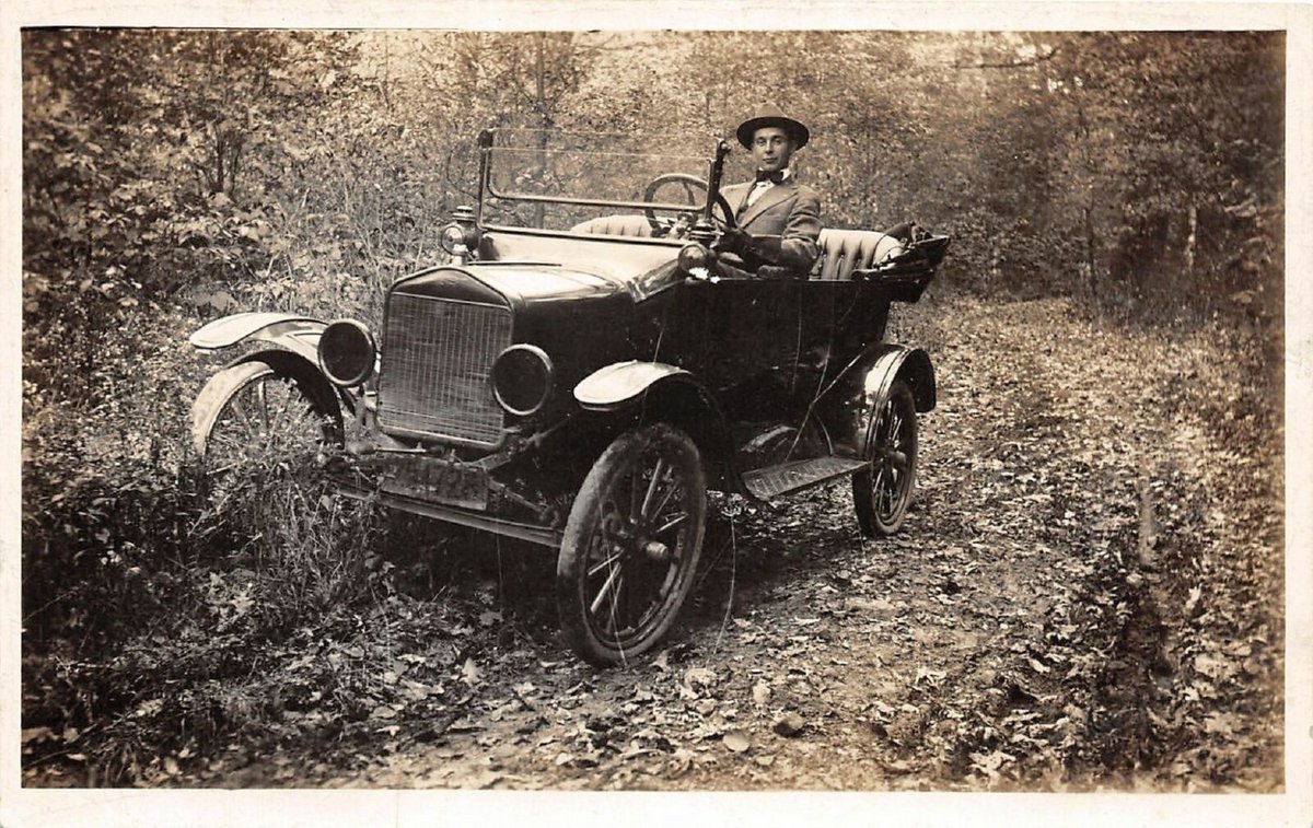 Old photo of a man sittting in one of the first build cars.